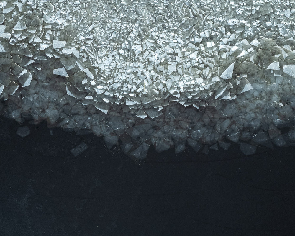 Närbild av isformationer på en mörk vattenyta, med kristalliknande iskristaller som sprider sig från toppen av bilden.