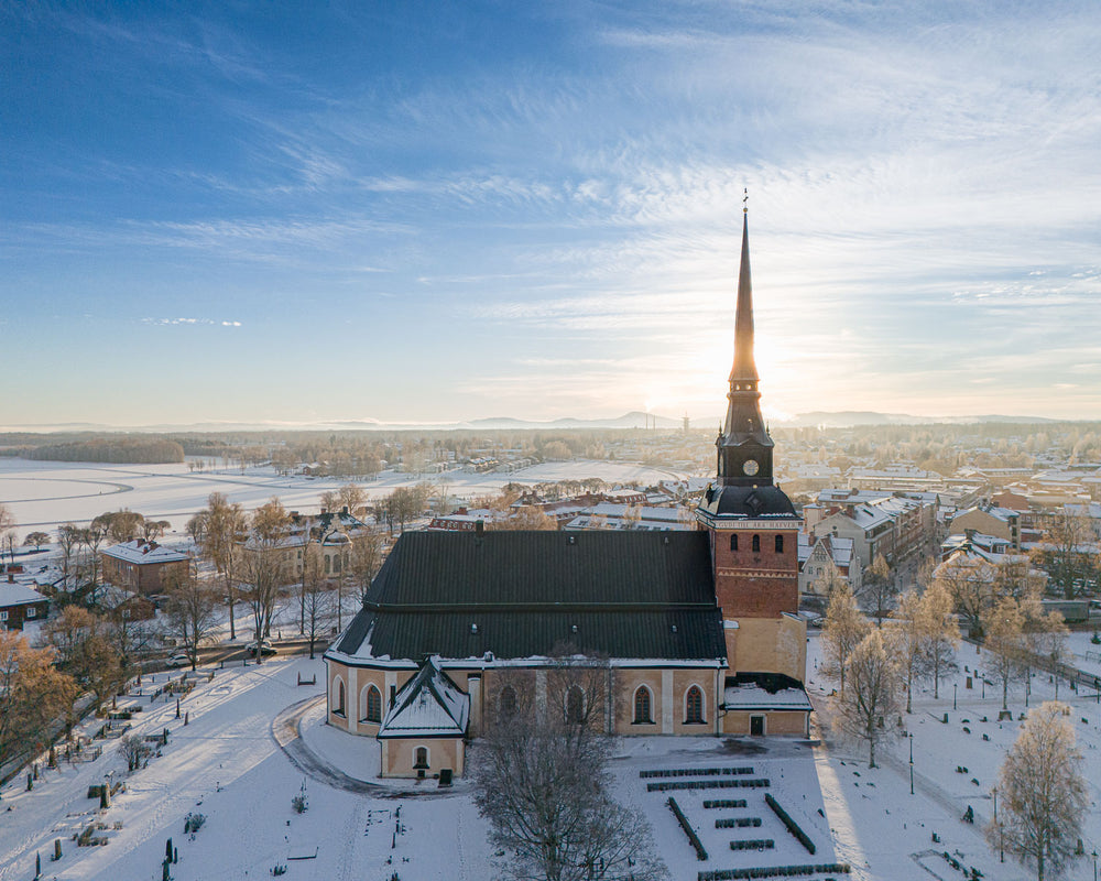 Drönarfoto över Mora kyrka i vinterlandskap med Siljan i bakgrunden och soluppgång över Mora stad.